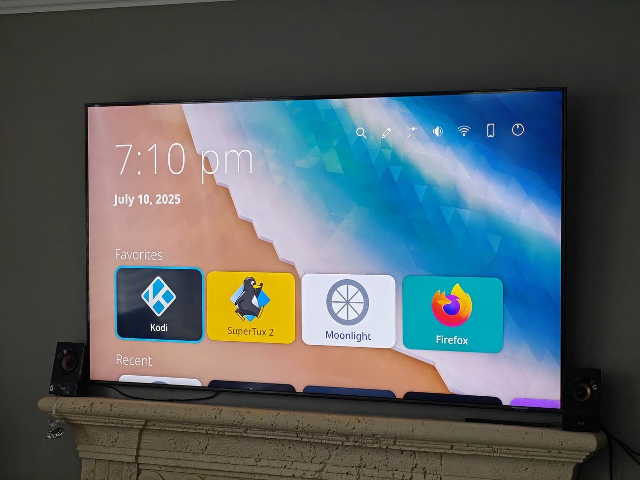 a photo that shows a big tv running the newly updated kde plasma bigscreen, the device is sat on a mantle, with two small external speakers beside it