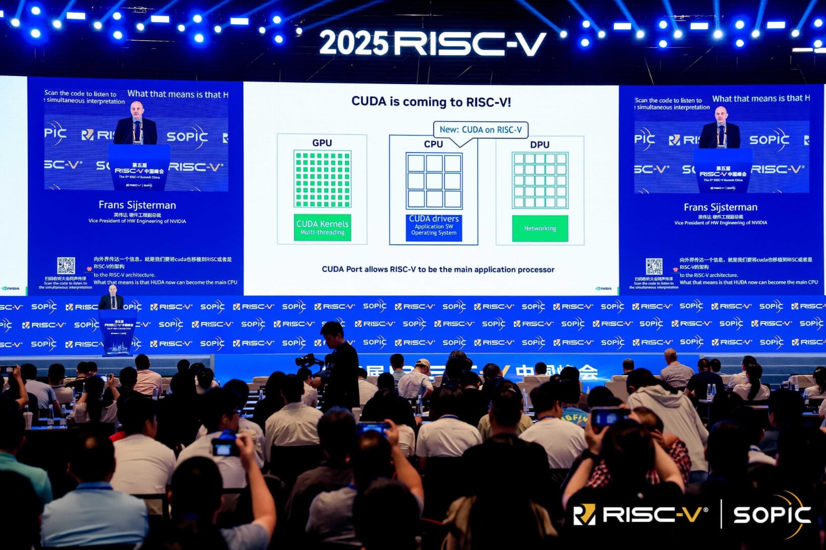 a photo that shows many people sat in the audience in front of a big stage with a wide screen on it, the screen is showing a presentation on the topic: cuda is coming to risc-v!