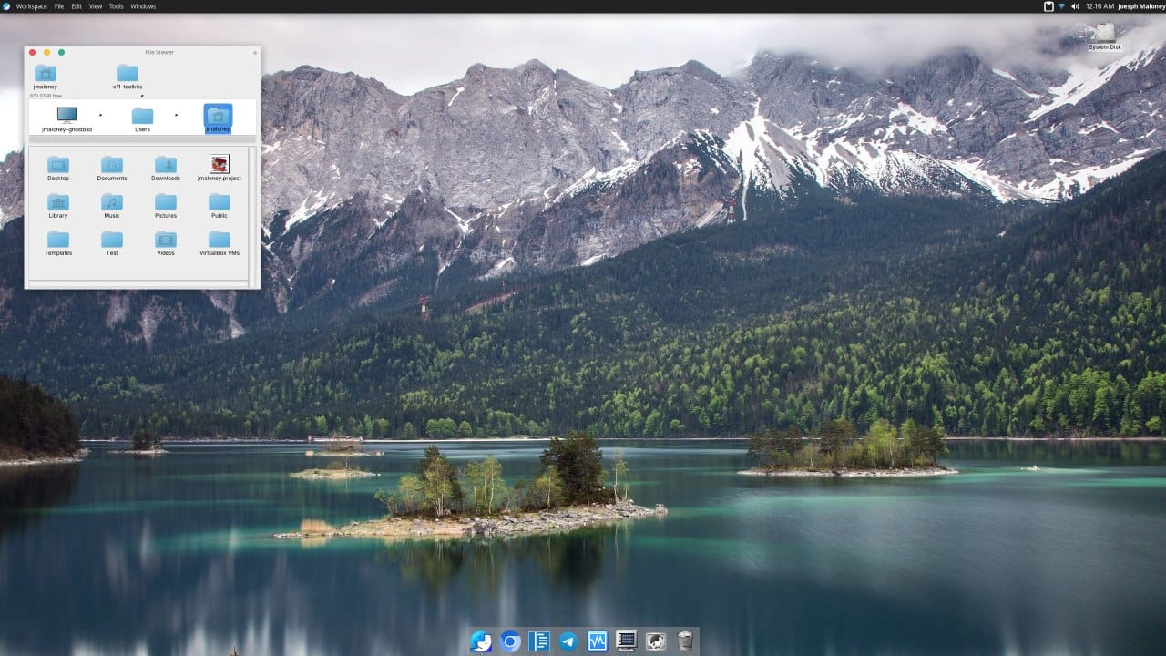 the desktop view of gershwin desktop environment is shown with a os x (macos) style interface with a dock at the bottom and a top bar, the wallpaper shows a snowcapped foresty mountain region with a lake in the middle