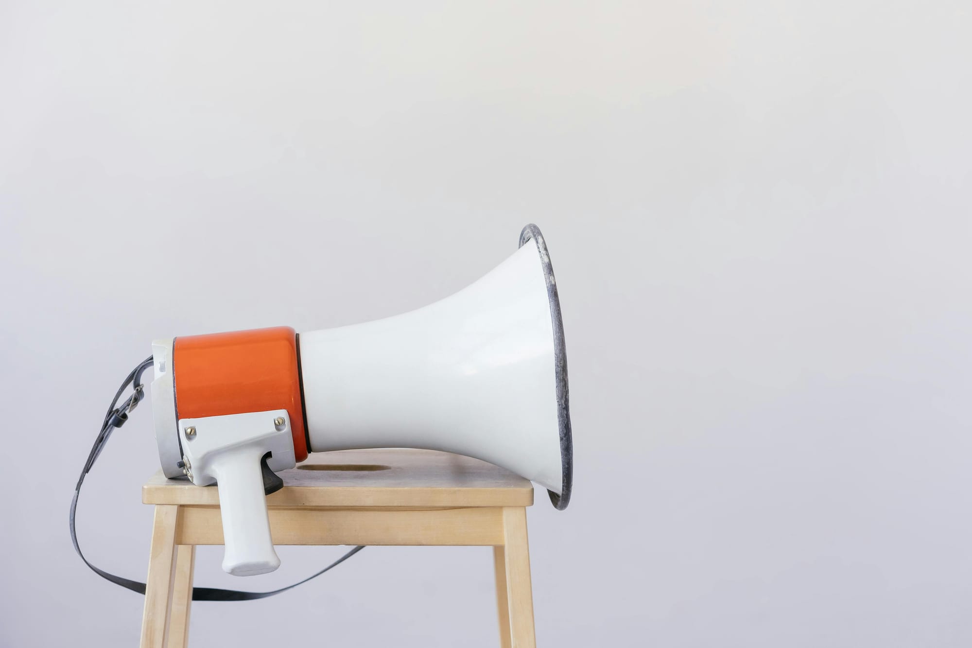 A photo of a loudspeaker with an orange base, white hand, and white flange with a silver rim, sitting on a lightly coloured stool