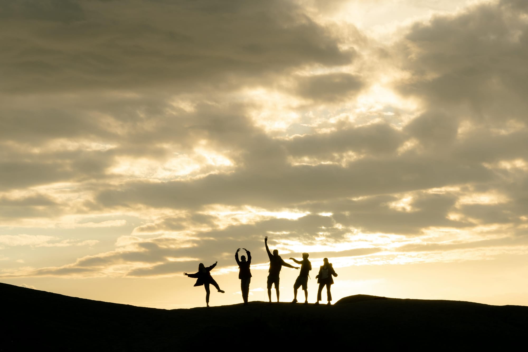 A silhouette of 5 person posing in front of a sunset sky while standing on what appears to be a hill